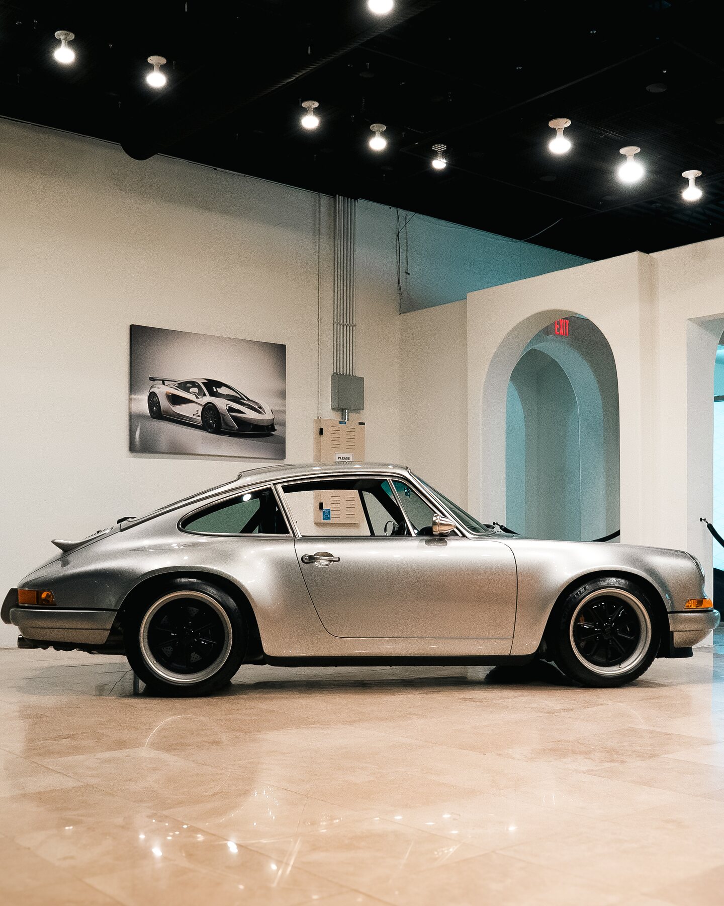 Full side profile of a silver Porsche 911 inside a private automotive gallery.