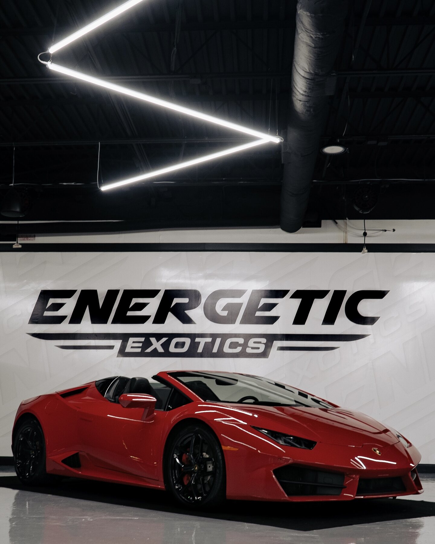 Red Lamborghini displayed beneath the Energetic Exotics showroom sign.