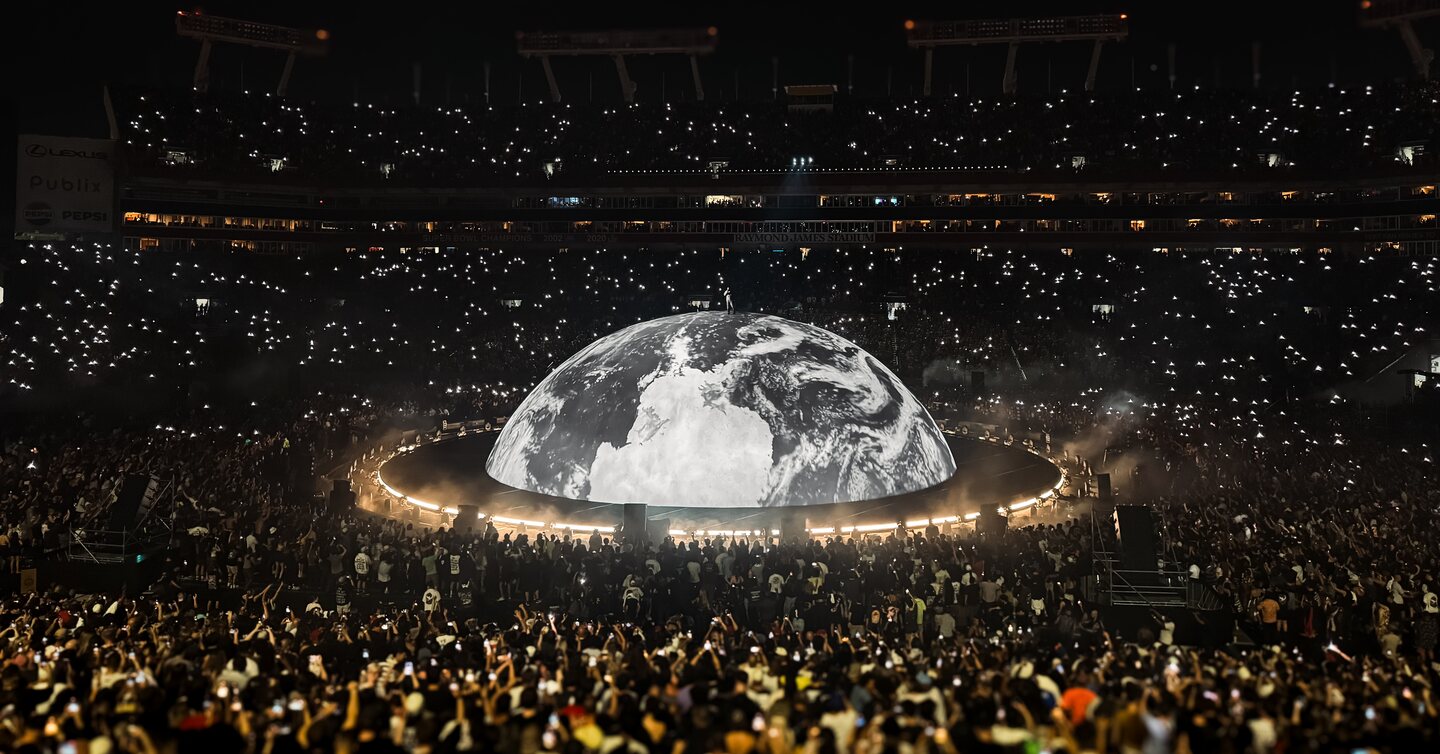 A stadium crowd surrounds an illuminated globe during a large production.