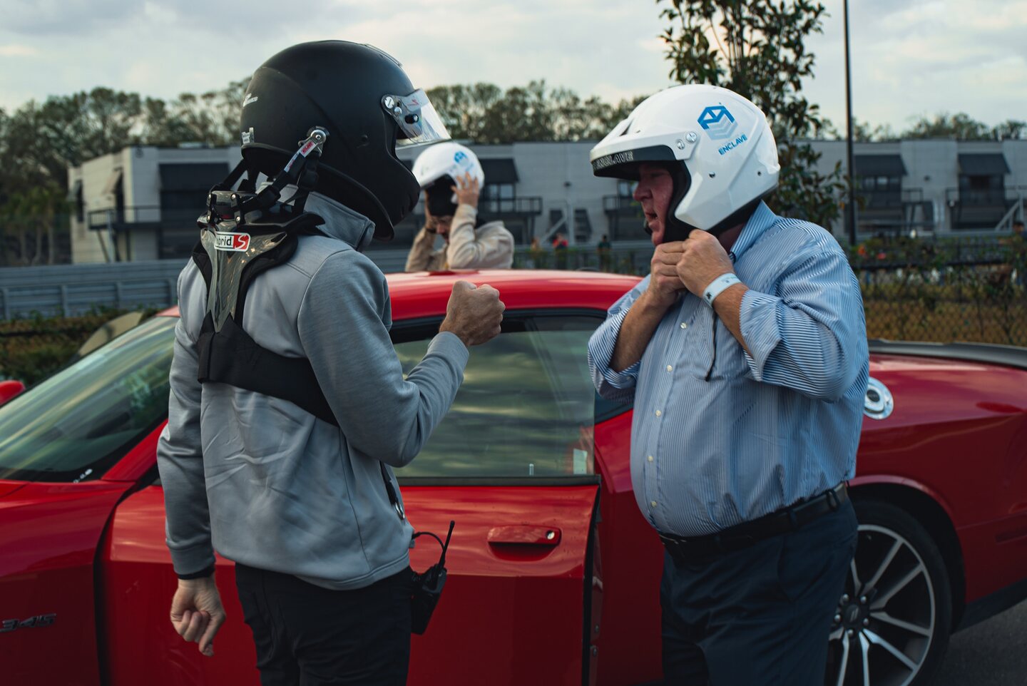 Drivers preparing their helmets beside a red car before going on track.