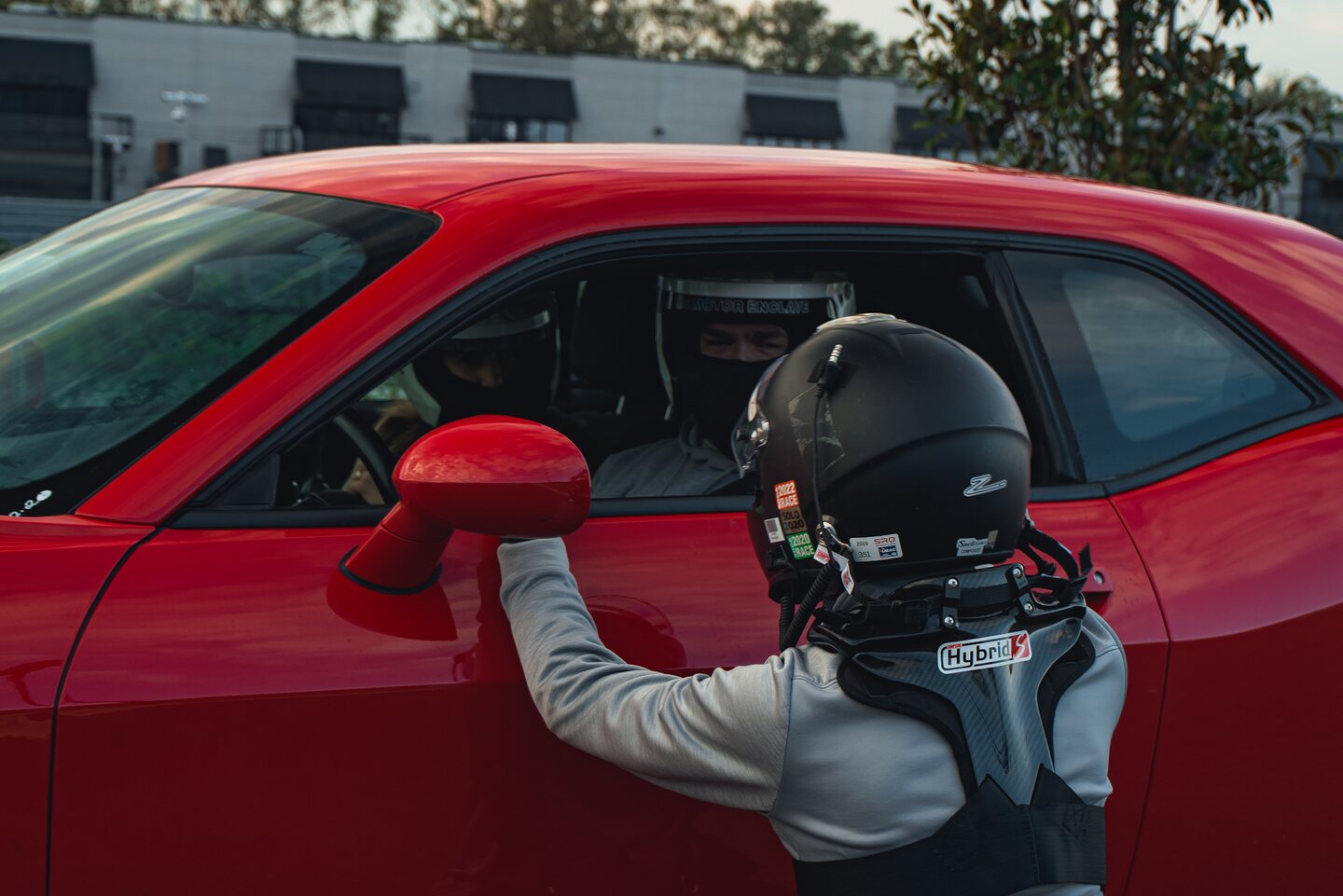 A helmeted driver speaking with the occupant of a red car on the grid.