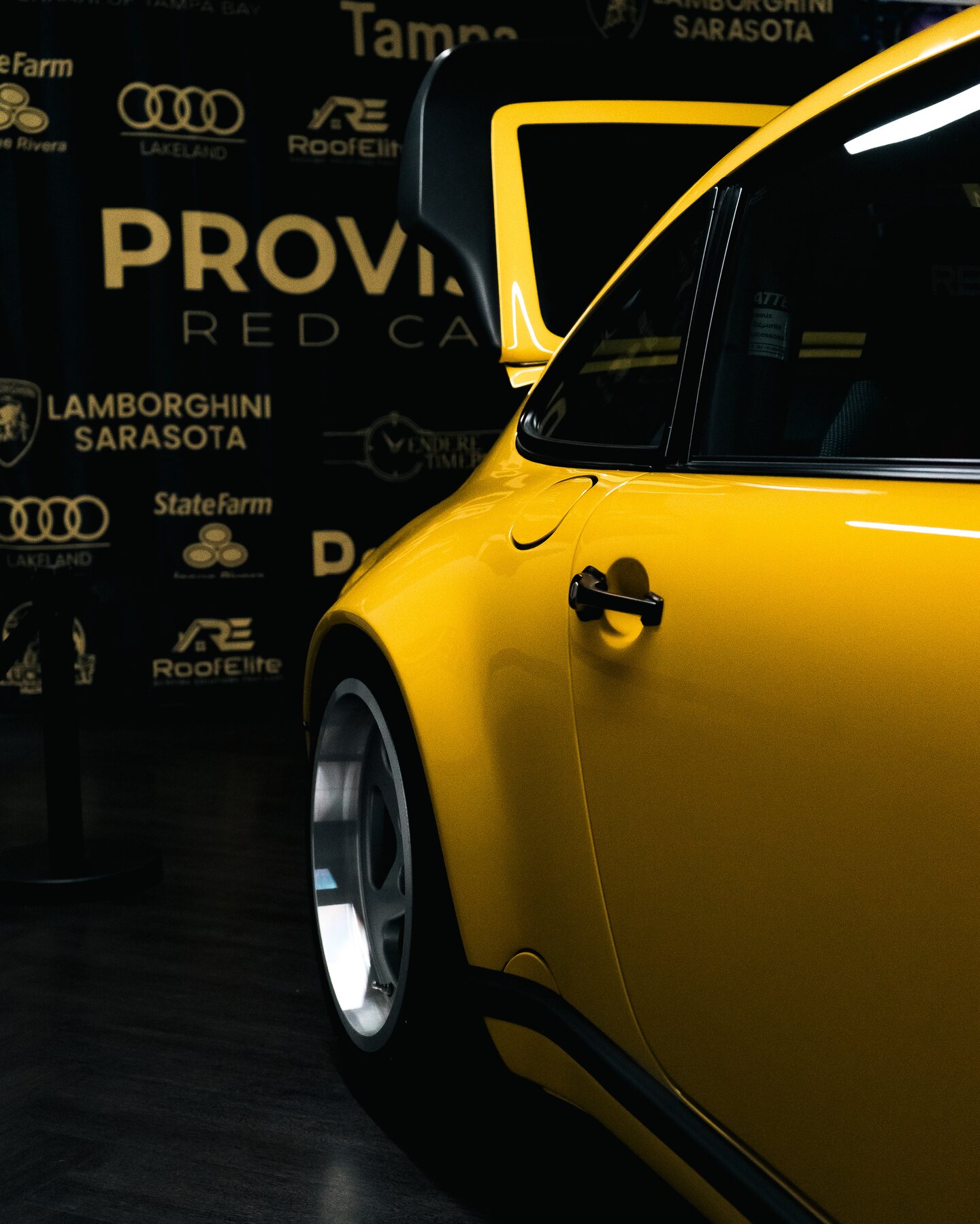 A yellow Porsche photographed beside the Provisions red carpet backdrop.